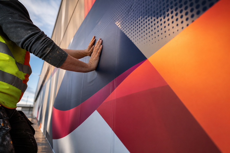 Installer applying large-format brand graphic to architectural wall during on-site environmental graphics installation